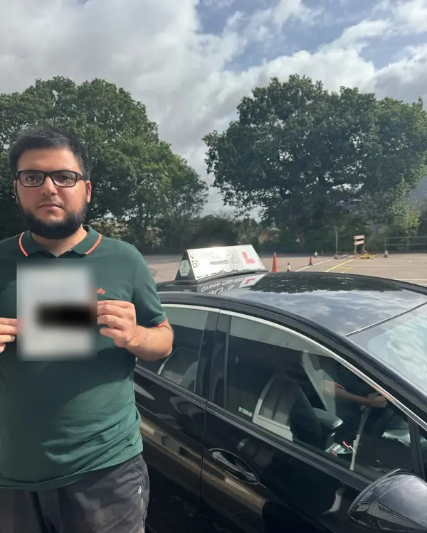 A learner holding their driving test pass certificate next to a Pass with Taj car