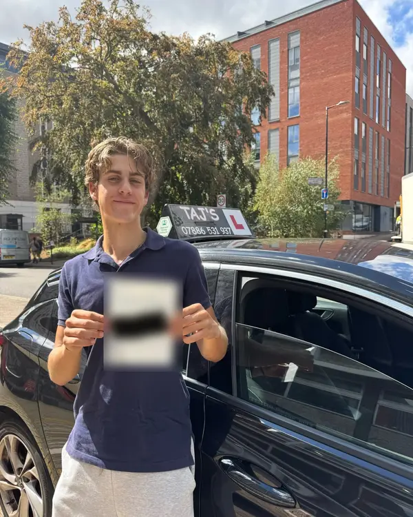 A learner holding their driving test pass certificate next to a Pass with Taj car