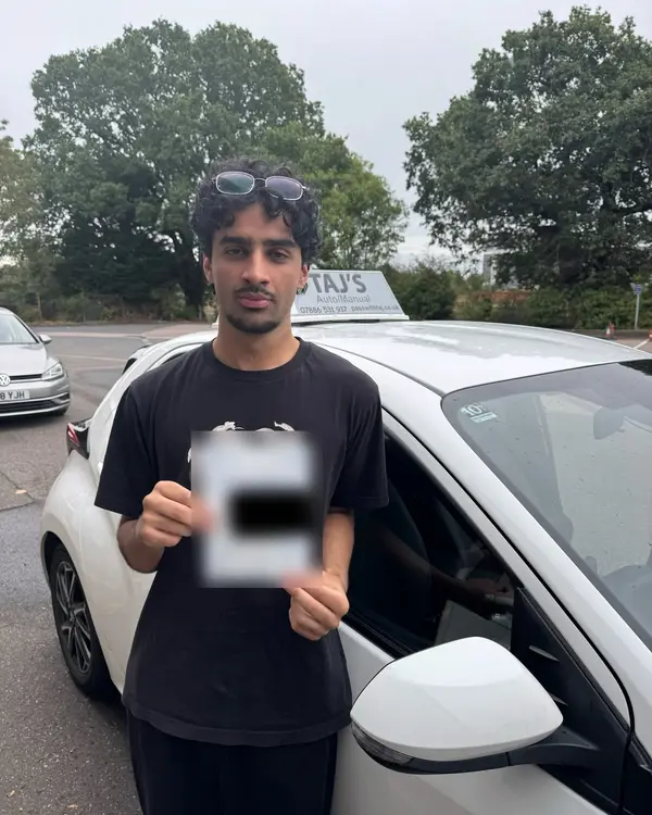 A learner holding their driving test pass certificate next to a Pass with Taj car